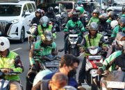 Seorang pengemudi ojek daring sedang menatap layar ponselnya saat menunggu pesanan di pinggir jalan Jakarta.